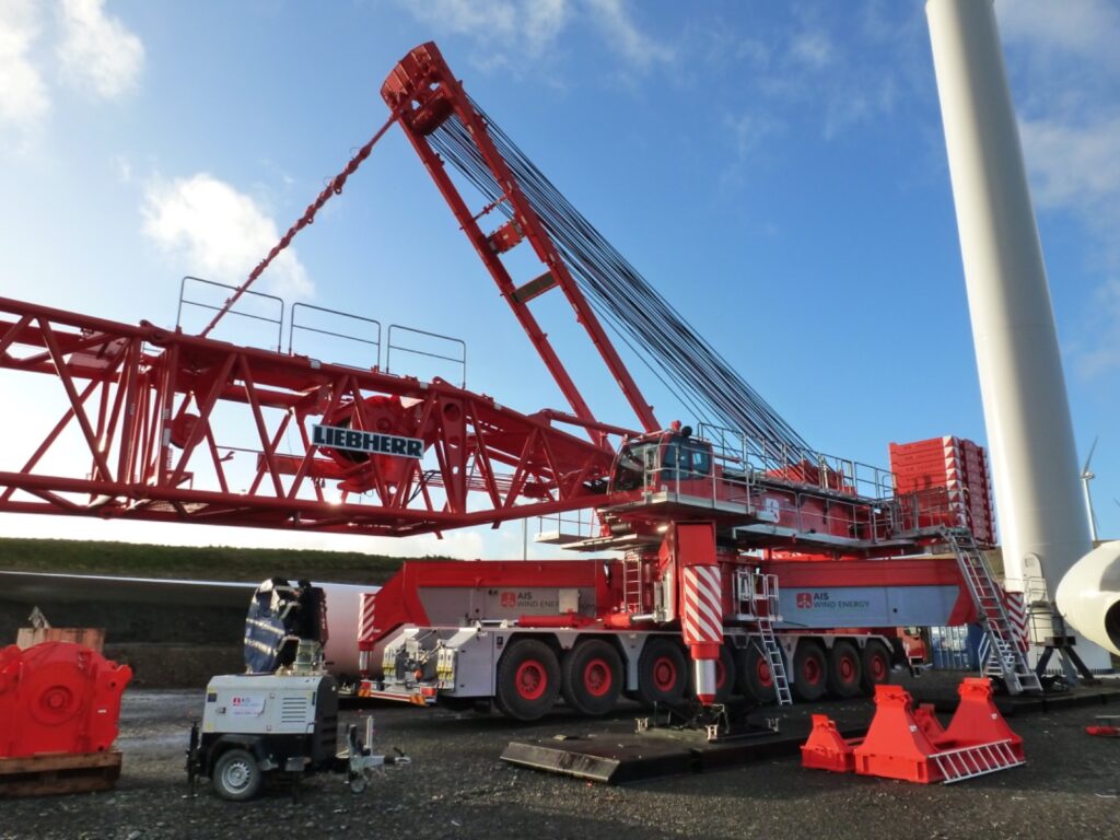 Red mobile crane being rigged beside a wind turbine tower on site